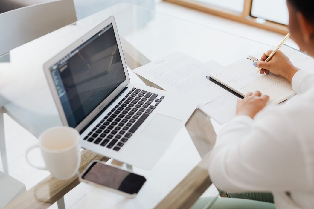 A person taking handwritten notes beside an open laptop during a call
