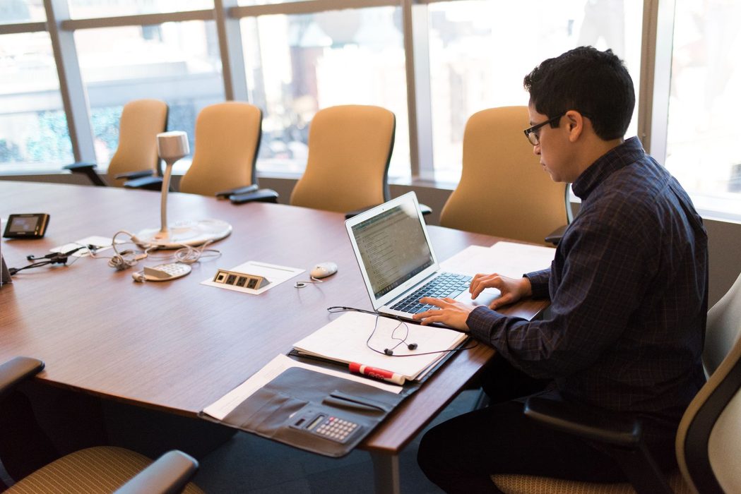 A person working at a laptop in a bright office, writing notes about a video call workflow