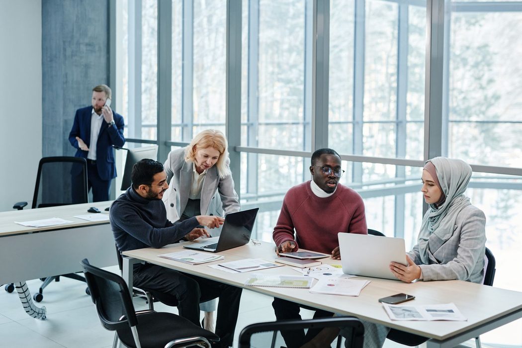 Four colleagues around a conference table with laptops and a wall screen